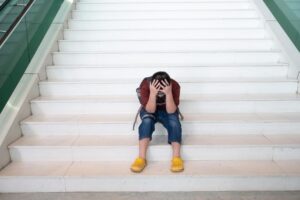 Adolescente na escada com as mão na cabeça olhando para baixo
