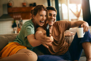 Casal sorrindo e assistindo filme juntos sentados no sofá