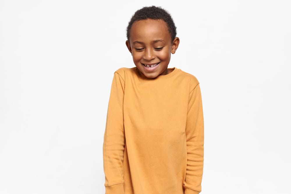 Menino com o sorriso tímido e ombros levemente levantados