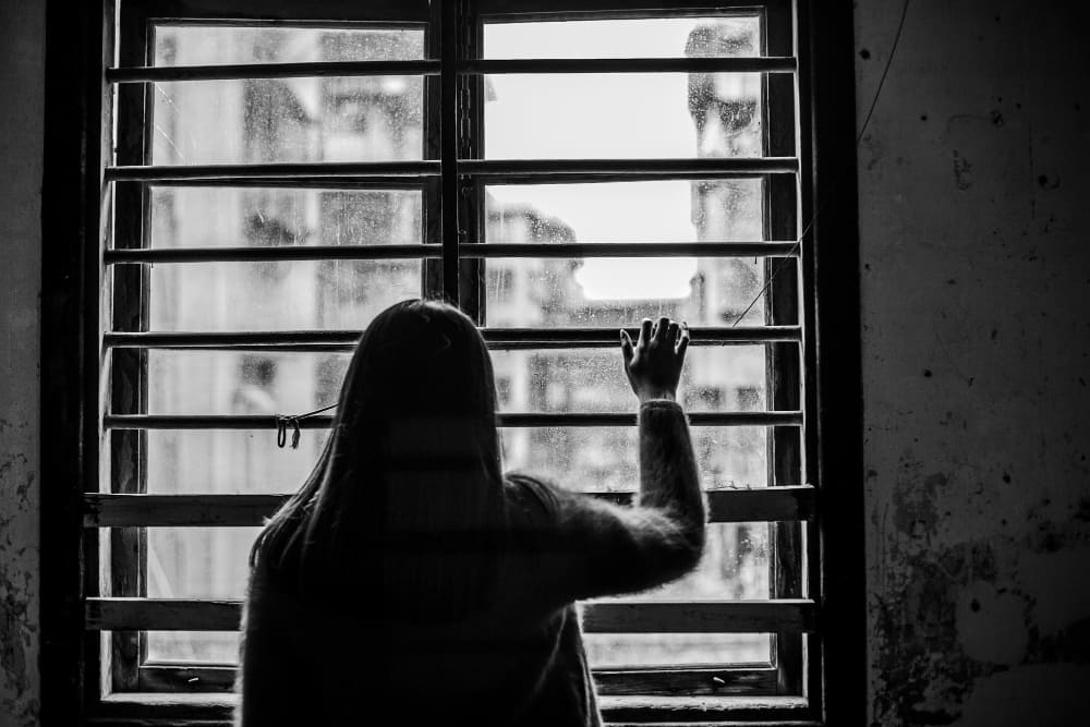 Mulher olhando o tempo chuvoso pela janela com tristeza