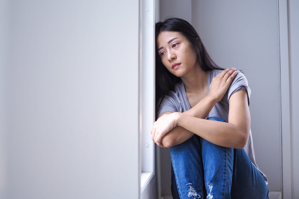 Mulher sentada no chão encostada na parede com semblante triste