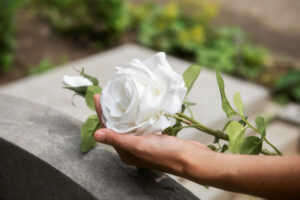 Pessoa segurando flor branca perto de um tumulo para mostrar fases do luto