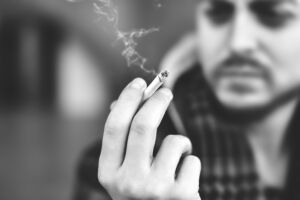 Homem segurando um cigarro, olhando para ele. Está pensativo.